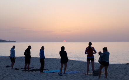 Teilnehmende machen Yoga zum Sonnenaufgang am Strand
