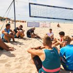 Teilnehmende des Beachvolleyball Camps in Sylt sitzen im Kreis um den Trainer am Strand