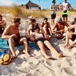 Teilnehmer sitzen am Strand neben dem Beachvolleyballfeld und lachen