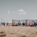 Teilnehmende sitzen neben dem Feld und schauen Beachvolleyball