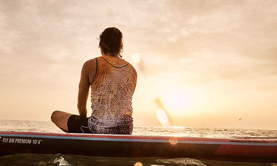 Mann sitzt auf Stand Up Paddle Board auf Sardinien beim Sonnenuntergang