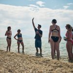 Gruppe steht im Wasser und Trainer erklärt Beachvolleyball