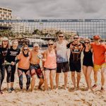 Gruppe von Trainern und Teilnehmende in einer Reihe vorm Beachvolleyballnetz