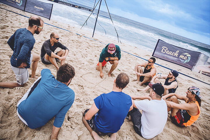 Beachvolleyball Trainer malt etwas in den Sand um Teilnehmern des Beachvolleyball Camps etwas zu erklären